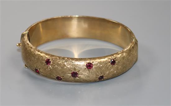A modern 9ct gold and garnet set hinged bangle, gross 28.3 grams.